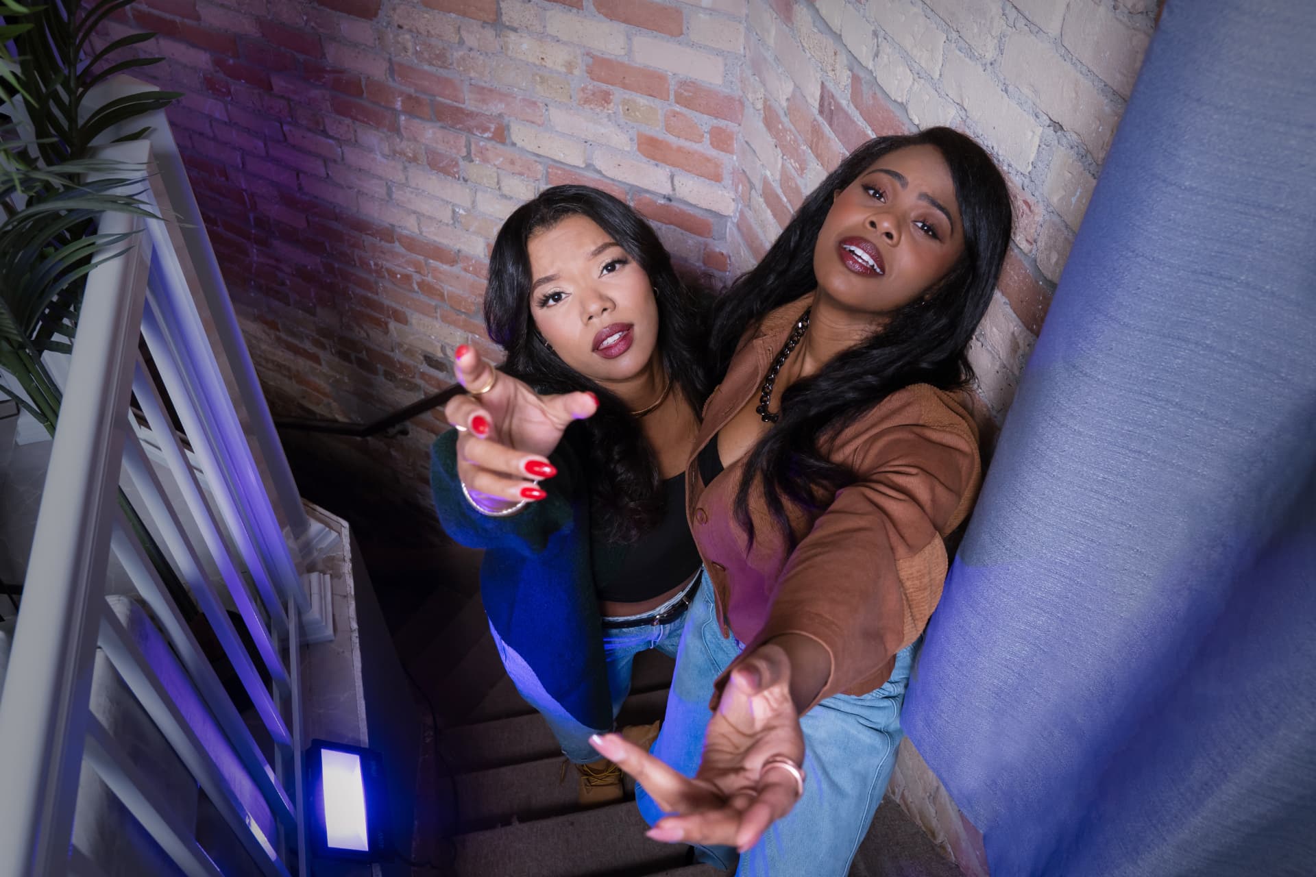 Shawna Stewart and Jayne Kamara reaching toward the camera on a stairwell
